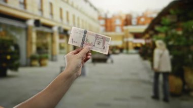 Şehrin arka planında bulanık yayaların olduğu bir sokakta elinde Suudi riyal banknotları tutan adam, açık havada finansal konsepti resmediyor..
