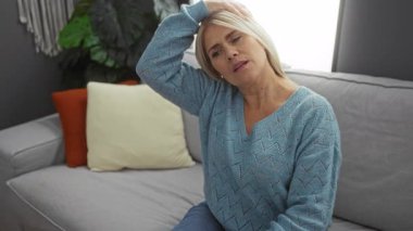 Rahat bir oturma odasında, kanepede uzanan mavi kazak giyen bir kadın evde rahatlama gösteriyor..