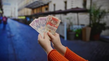 Şehir arka planında bulanık şehir manzarası olan şehir caddesinde Kolombiya pezosu tutan kadın elleri, açık hava ticaretini yansıtıyor..