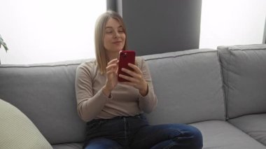 Kadın ve erkek rahat bir oturma odasında akıllı bir telefonla koltukta oturuyor ve modern dekorlu rahat ve samimi bir ortam sergiliyorlar..