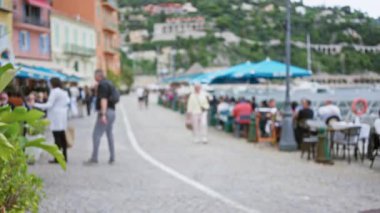 Pahalı villefranche-sur-mer gezinti alanı boyunca yürüyen insanlar, yumuşak odaklı şehir manzarasında canlı kafeler ve manzaralı liman, açık hava ortamı ve turizmi vurguluyor..