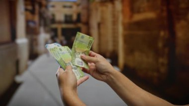 Şehir sokaklarında Şili pesolarını sayan bir adam, açık havada yatırımları ve iş faaliyetlerini ön plana çıkarıyor.