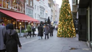 Şenlikli Londra caddesinde kışın Noel ağacı ve süslemelerle yürüyen bulanık figürler..