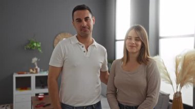 Oturma odasında gülümseyen bir çift, kadın ve erkek evlerinin yakınında duruyor. Kapalı bir yerde sıcak ve sevgi dolu bir atmosfer yaratıyorlar. Doğal ışık ve rahat bir dekor..