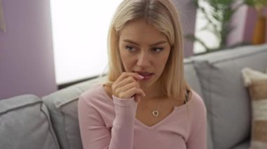 Sıcak bir oturma odasındaki kanepede tırnaklarını yiyen bir kadın endişeli görünüyor..