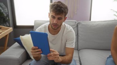 Modern oturma odasındaki kanepede oturup tablet kullanan ve birlikte gülen çift evde eğleniyor..