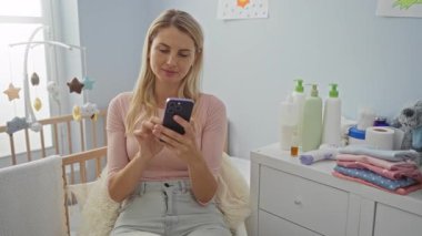 Bebek odasındaki rahat telefonu kullanan bir kadın. Şifoniyerinin üzerinde bebek eşyaları ve beşik var.. 