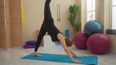 Spor salonunda yoga yapan kadın spor topları ve bitkilerle kapalı alanda sakinleştirici bir ortam yaratıyor..