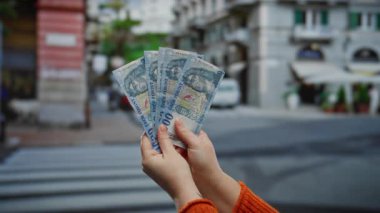 Bir şehir caddesinde elinde Macar banknotları tutan bir kadın, açık hava ortamında para gösteriyor..