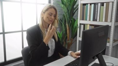 Ofiste oturan kadın bilgisayarına bakarken, arka planda bitkiler ve kitaplıkla geniş pencereli modern iş ortamında strese giriyor.. 