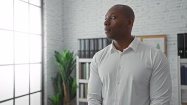 Kendine güvenen adam modern bir ofiste rafları, bitkileri ve parlak pencereleri olan, profesyonellik ve başarı saçan kollarını kavuşturdu..