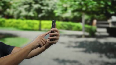 Parkta akıllı telefon kullanan ve elleri odak noktasında bulanık bahçe arkaplanı açık hava aktivitesi dijital cihaz teknolojisi yaşam tarzını ön plana çıkaran bir adam.