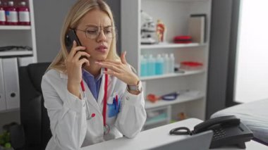 Beyaz önlüklü kadın telefonda konuşuyor. Elinde malzeme rafları var. Klinik ortamında doktor ya da sağlık uzmanı olduğunu gösteriyor..