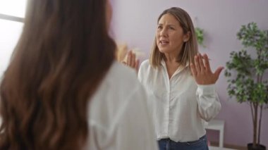 Parlak oturma odasında kızıyla konuşan kadın, konuşma sırasında duygularını ifade ediyor, aile dinamiklerini ve sevgiyi modern bir ev ortamında, kapalı mekanlar ve hafif ışıklandırmalarla tasvir ediyor..