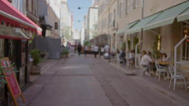 Marsilya 'da güneşli bir gökyüzü altında bulanık kafeler, insanlar ve mimari ile sokak sahnesi, Fransa' daki kentsel yaşamın özünü yakalıyor..