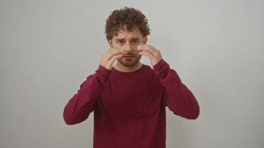 İspanyol tişörtlü genç adam şok olmuş bir ifadeyle ayakta duruyor ve izole edilmiş beyaz arka plan üzerinde şaşkın bir yüz ifadesi var.