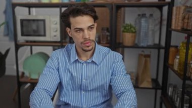 Ofisteki çizgili gömlekli genç adam iç mekan bitkileri ve ofis eşyalarının arasında işe odaklanmış, düşünceli ve çevreyle iç içe geçmiş görünüyor..