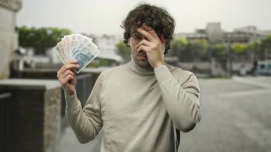 Şehir sokaklarında yaşayan İspanyol bir adam, kentsel çevredeki mali stresi sembolize ederek Polonya 'nın zloti banknotlarını endişe içinde tutuyor..