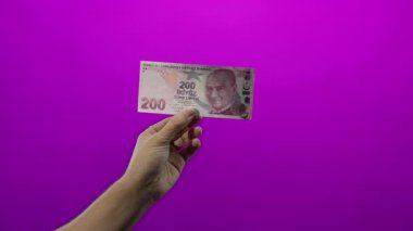 Duvarın üzerinde izole edilmiş mor arkaplan üzerinde Türk lirası banknotları tutan adam, hisse senetlerinde canlı renk kontrastı olan finansal kavramları yakalıyor.