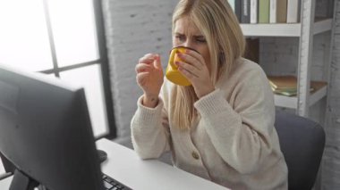 Ofiste çalışan bir kadın, rahat ve modern bir ortamda kahve içerken bilgisayarda daktilo kullanıyor.