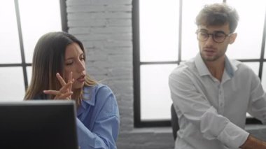 Dizüstü bilgisayarı olan kadın ve erkek, modern bir işyeri içinde çalışma, takım çalışması ve profesyonel ortamda potansiyel iş gerilimi konularını tartışırken stresli görünüyorlar..