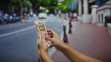 Arka planda arabaların geçtiği bir şehir sokağında elinde Çin Yuanı banknotları tutan adam..