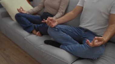 Bir çift, rahat bir oturma odasındaki rahat bir kanepede birlikte meditasyon yapıyor. Huzuru kucaklayan rahat bir erkek ve kadın var..