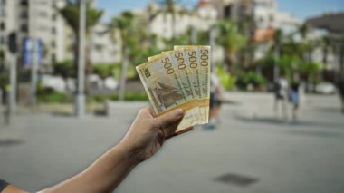 Şehir caddesinde elinde Norveç kronu banknotları, bulanık yayalar, açık havada paralı bir şehir adamını hareketli bir sokak arkaplanına karşı sergiliyor..