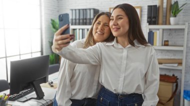 Parlak bir ofis ortamında selfie çeken kadınlar, kapalı bir iş ortamında kadın çalışanlar arasında takım çalışması ve arkadaşlık gösteriyorlar..