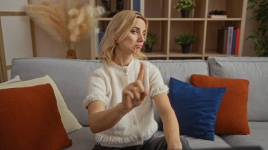 Modern dekorasyonla şık bir oturma odasında renkli yastıklı, rahat bir dairede parmağını gösteren bir kadın..