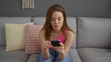 Evdeki koltukta oturan bir kadın modern bir oturma odasında akıllı telefon kullanıyor.