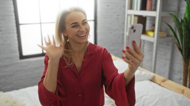 Sıcak yatak odası ortamında gülümseyen bir kadın, kırmızı pijama giyiyor, arka planda parlak bir pencere var, rahat bir sabah atmosferi sergiliyor..