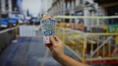 Arka planda inşaat ve şehir ortamındaki yatırımları sembolize eden, şehir sokaklarında Meksika pezosu tutan bir adamın eli..