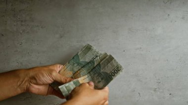 Elleri beton bir arka planda Endonezya rupiası tutuyor.