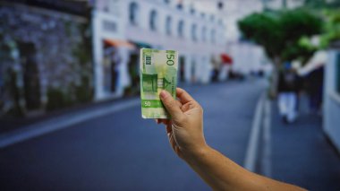 Kentsel bir sokakta Norveçli kronu elinde tutan adam, şehir ortamında iş ve yatırım kavramlarını temsil ediyor..