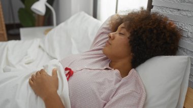 Yatak odasında kıvırcık saçlarıyla uyuyan bir kadın evde rahatlık ve rahatlığı yansıtan sakin bir atmosferi yakalıyor..