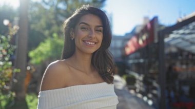 Güneşli bir günde şehir parkında gülümseyen bir kadın, şehir sokaklarında canlı, neşeli bir atmosfer ve güzellik sergiliyor..