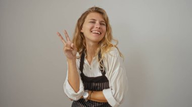 Önlüklü çekici sarışın kadın beyaz arka planda izole edilmiş barış işareti gösteriyor.