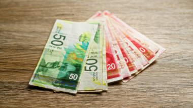 İsrail şekelleri ahşap bir yüzeye yerleştirilmiş, canlı İsrail para birimi kapanışı sergiliyor, hem 50 hem de 20 şekel banknotlar vurgulanıyor..