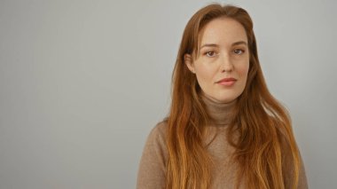 İzole edilmiş beyaz arkaplanda, kızıl saçlı bir kadın kameraya özgüvenli bir şekilde bakıyor. Basit bir ortamda zarafet ve çekici özellikler gösteriyor..