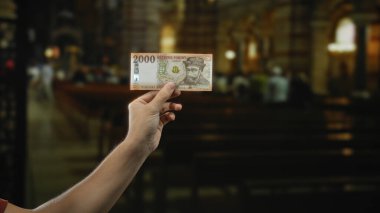 Kilisenin arka planında bulanık olan, kültürel ve finansal temaları vurgulayan Macar banknotları tutan bir adam..