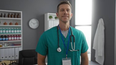 Hastanedeki genç adam, yeşil önlük giyip, steteskopla güvenle gülümsüyor. Parlak kliniğin iç kısımlarında, profesyonel sağlık hizmetlerini öneriyor.