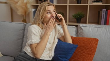 Telefonda konuşan bir kadın, şık bir oturma odasında koltukta, bej renkli bir kazakla olgun güzelliğini ve modern dekorunu sergileyerek şaşırdı..