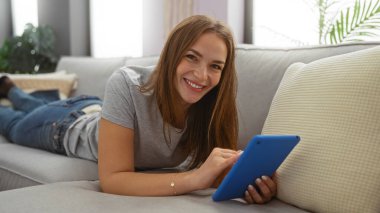 Rahat bir oturma odasında tablet kullanırken evde gülümseyen bir kadın, evdeki dijital bağlantıya odaklanmış rahat ve modern bir yaşam tarzı sergiliyor..