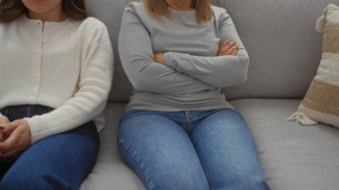 Anne ve kızı sıcak bir oturma odasında kollarını kavuşturmuş bir kanepede oturuyor. Aile içi gerginliği ve bağları tasvir ediyorlar..