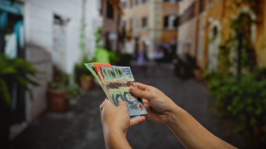Bir şehir caddesinde Avustralya doları tutan bir adam, açık hava ortamında çeşitli banknotlar sergiliyor, döviz borsasını veya iş alım-satım temalarını vurguluyor.