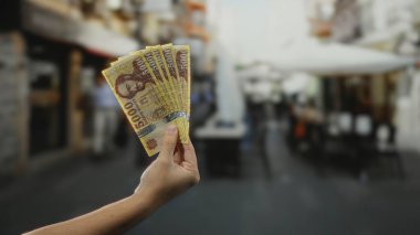 Kalabalık bir şehrin arka planında el ele tutuşan Macar banknotları. Yoğun bir atmosferi ve uzak mesafede bir adamı olan açık bir şehir manzarası..