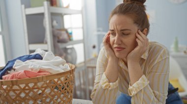 Çamaşırhanede bir kadın, düşünceli bir ifadeyle bir sepet kıyafete bakıyor, ev hayatının özünü çekici ve modern bir dokunuşla yakalıyor..