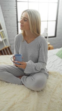 Yatak odasında rahat bir şekilde oturan, elinde kahve fincanı tutan, günlük şezlonglar giyen, camdan içeri gün ışığı süzülen bir kadın, evde rahat bir sabah geçirmeyi öneriyor..