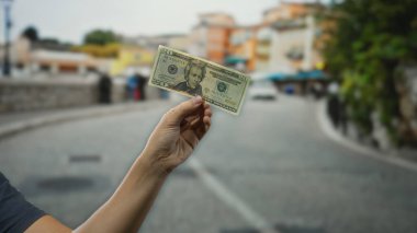 Bir şehir caddesinde elinde Amerikan Doları banknotuyla finans ve ekonomi sergileyen bir adam açık hava ortamında para ve ticareti vurguluyor..